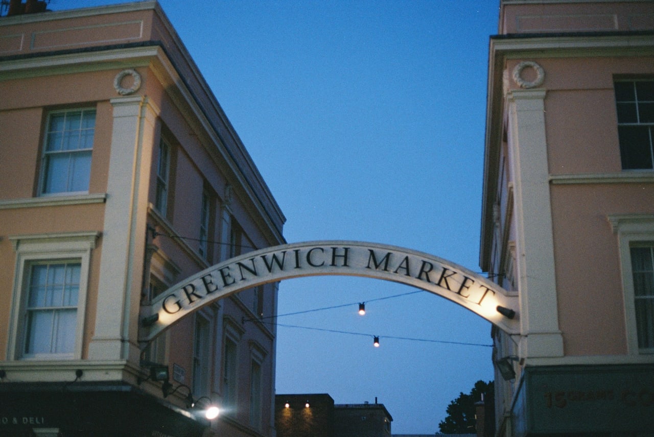 The arched Greenwich Market sign lit between buildings at dusk